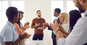 Group of clapping employees gathered around a single employee - providing incentives and benefits uplifts workplace culture