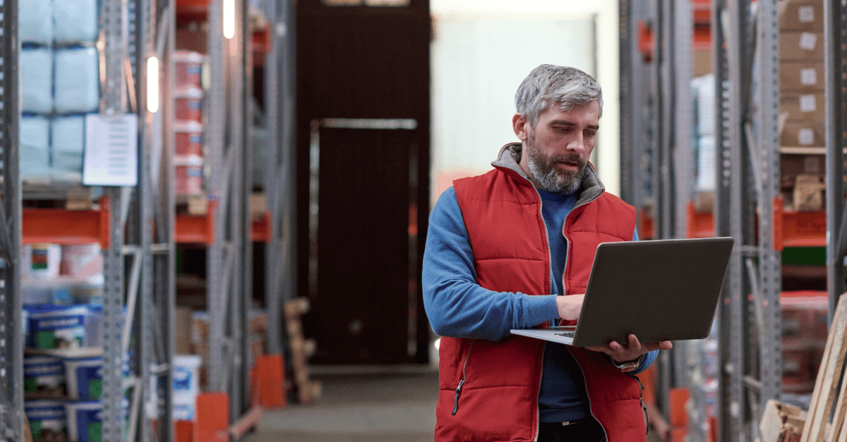 Rebate management software - Man in warehouse wearing red vest and using a laptop