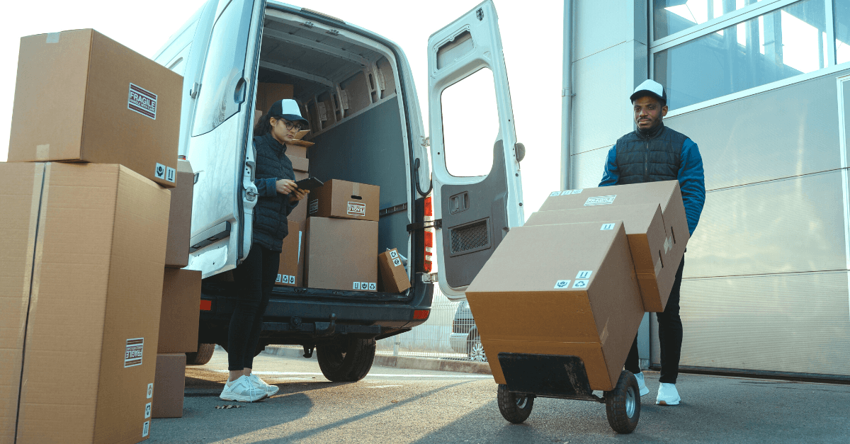 Two distribution professionals moving product boxes out of a van.