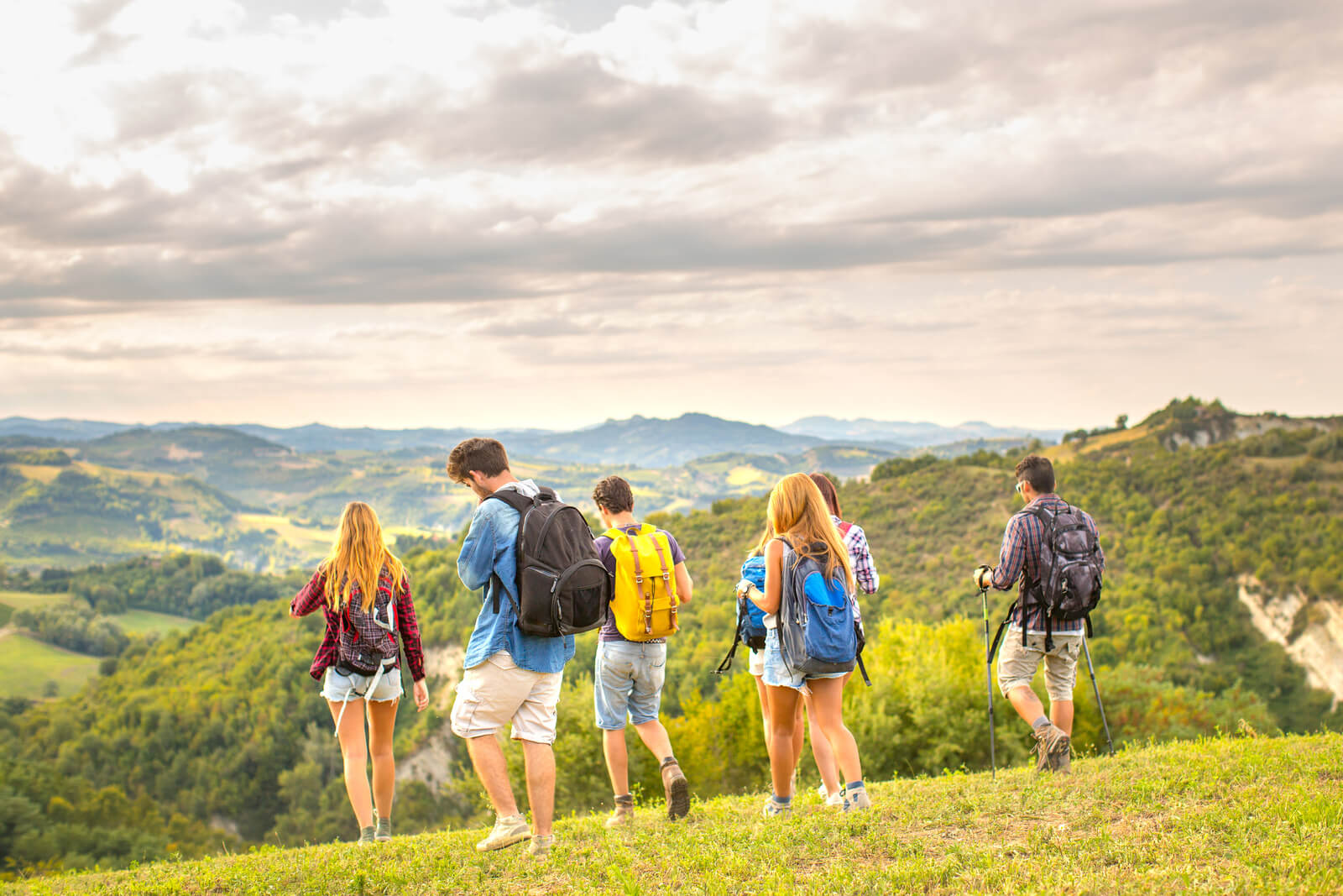A group of people wearing backpacks, walking through green hills - incentive travel services